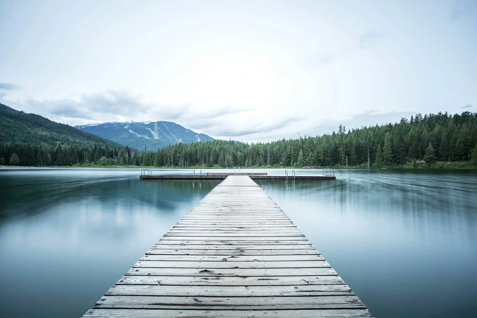A wooden dock stretching into a calm lake surrounded by forested mountains